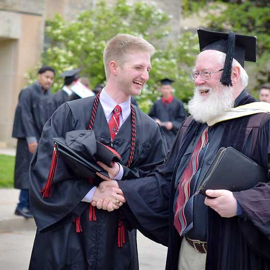 A graduate laughs with a professor as they prepare for Commencement
