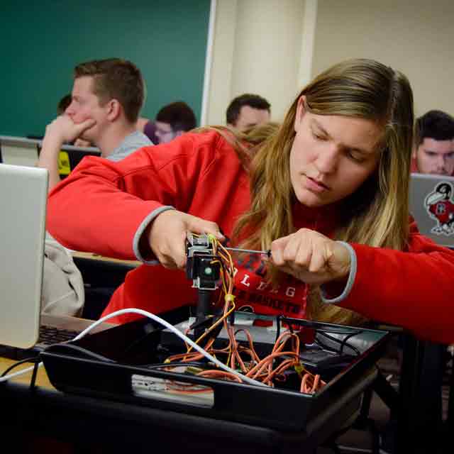 A female student in Engineering class works with a device in class.