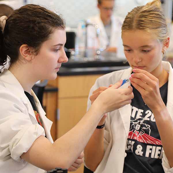 Two BCYC Immersion chemistry track students in lab coats analyzing test tube