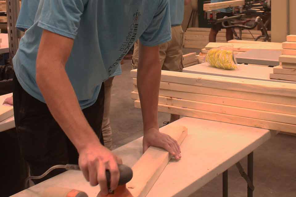 A student volunteer works with a sander and a piece of wood
