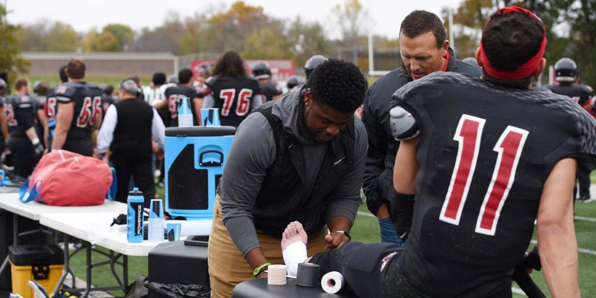 A student wraps a football student athlete's leg at a game