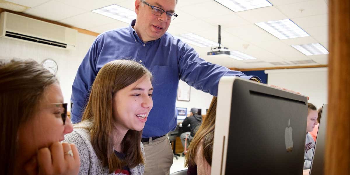 Professor Kevin Page works with students at a computer workstation