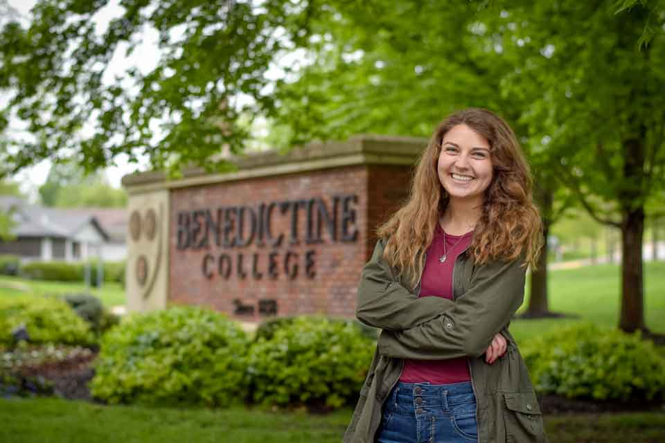 A student poses for a photo near the Benedictine College entrance sign