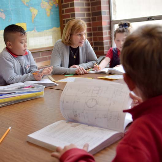 A teacher sits with young students at a table