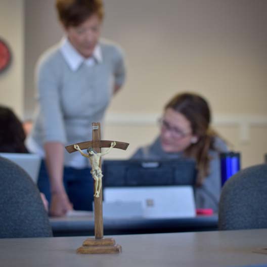 A Crucifix in the foreground with a student and graduate and teacher in the background