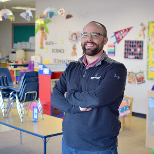 A graduate student standing in a school classroom