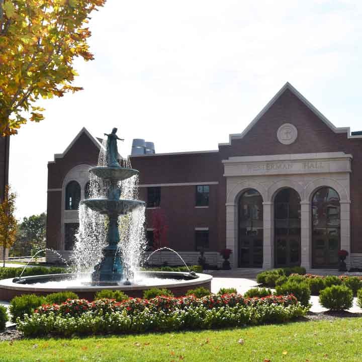 Our Lady of Grace Fountain surrounded by flowers with the Ferrell Academic Center in the background