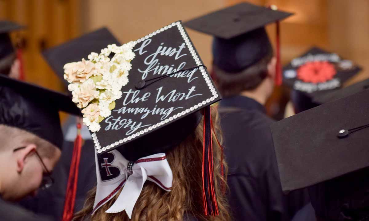 A Benedictine College graduate with a decorated hat that says "I just finished the most amazing story"