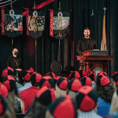 Freshmen in beanies listen to Father Simon Baker during the academic convocation