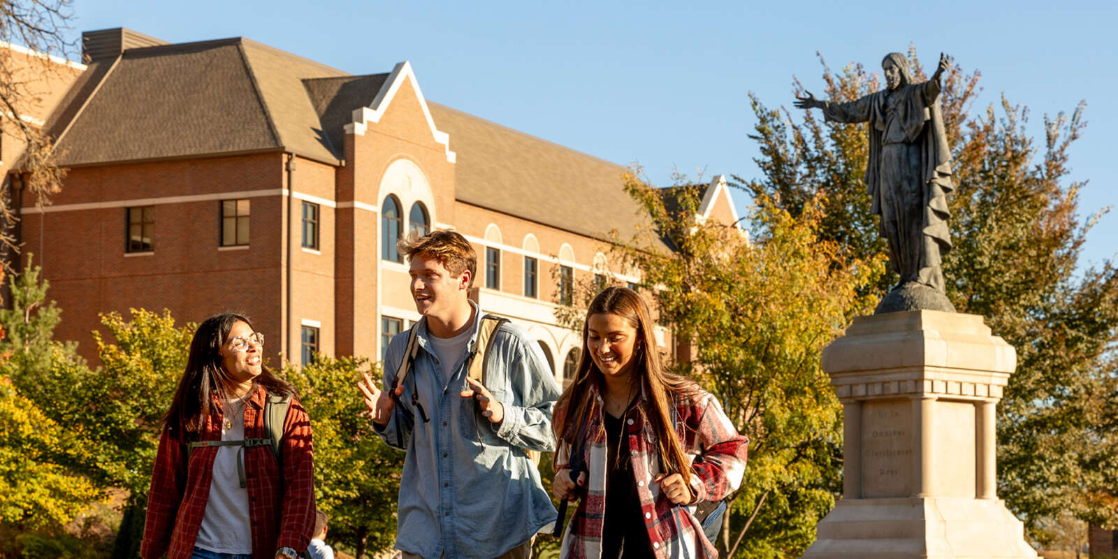 Students walking in Raven Memorial Park with the statue of the Sacred Heart of Jesus behind them