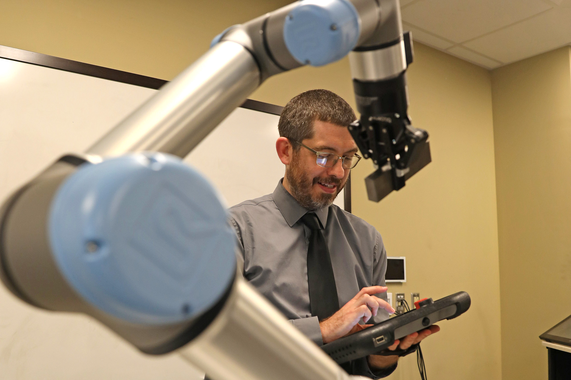 An engineering faculty member works with an industrial robot using a tablet