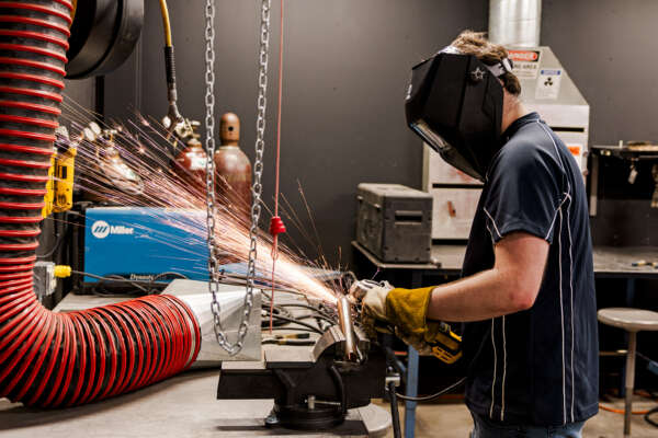 A person uses a grinder on a piece of metal in a vice