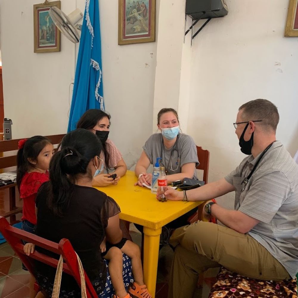 A group of people in masks have a conversation at a table