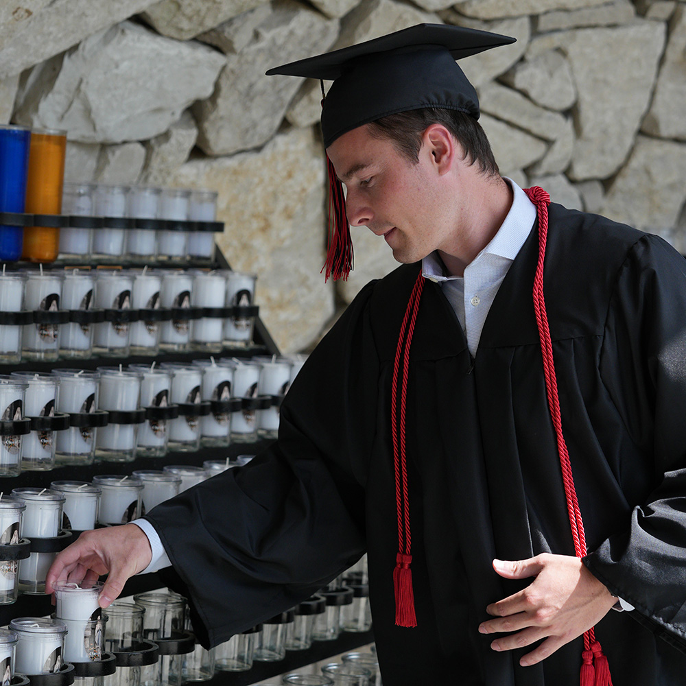 A graduate places a candle in Mary's Grotto during the March of Light