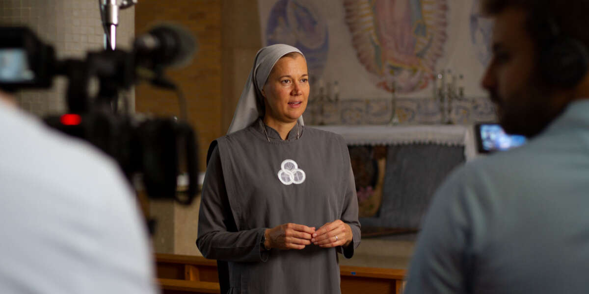 A religious sister speaks while a film crew records